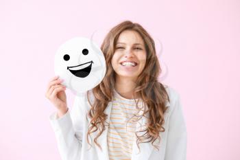 Portrait of happy young woman with emoticon on color background�