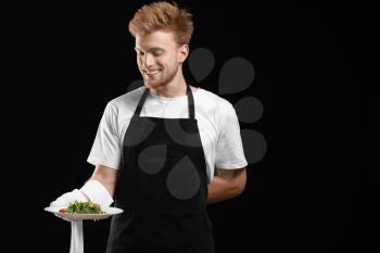 Handsome waiter with salad on dark background�