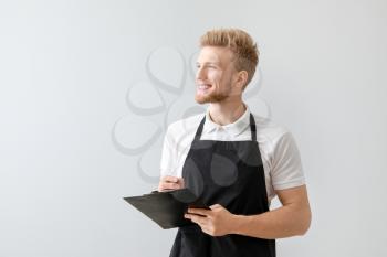 Handsome waiter with clipboard on light background�