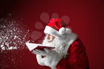 Portrait of Santa Claus with book blowing snow on color background�