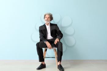 Fashionable senior man sitting on chair near color wall�