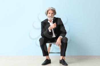 Fashionable senior man sitting on chair near color wall�