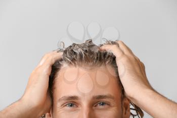 Handsome young man washing hair against grey background�