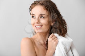 Beautiful young woman wiping hair after washing against grey background�