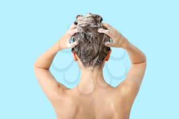 Beautiful young woman washing hair against color background, back view�