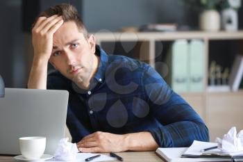 Stressed young man at table in office�