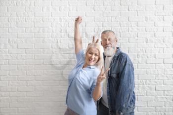 Happy mature couple showing victory gesture against white brick wall�