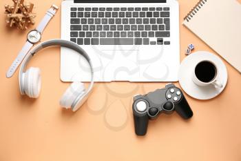 Laptop with joypad, headphones and cup of coffee on color background�