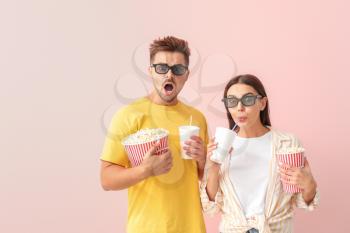 Emotional couple with popcorn and drink watching movie on color background�