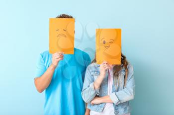 Young couple hiding faces behind emoticons against color background�