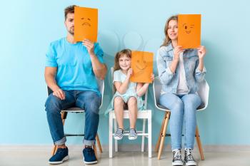 Young family with emoticons sitting on chairs near color wall�