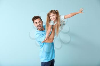 Happy father playing with daughter on color background�