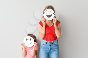 Mother and little daughter hiding faces behind emoticons against light background�