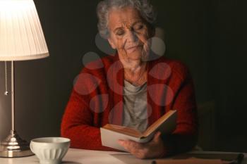 Senior woman reading book at night�