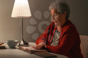 Senior woman reading book at night�