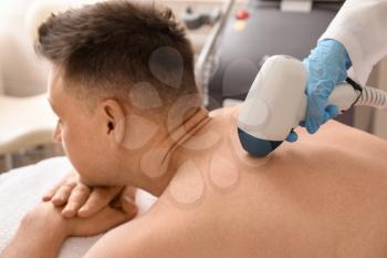 Handsome man undergoing procedure of laser hair removing in beauty salon�