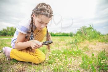 Little girl with magnifying glass studying nature outdoors�