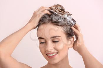 Beautiful young woman washing hair against light color background�