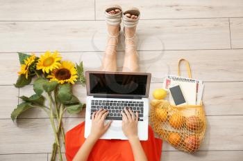 Woman with laptop, sunflowers and shopping bag sitting on floor, top view�