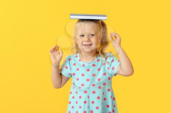 Cute little girl with book on color background�