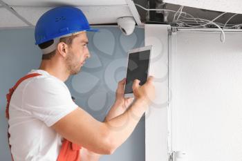 Electrician with tablet computer installing alarm system indoors�