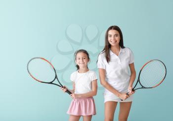 Little girl and her mother with tennis rackets on color background�
