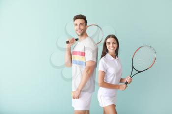 Young couple with tennis rackets on color background�