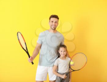 Little girl and her father with tennis rackets on color background�