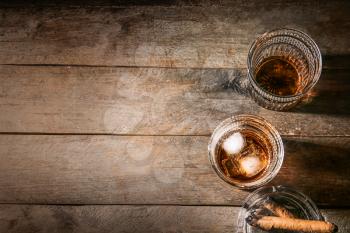 Glasses of cold whiskey with cigars on wooden table�