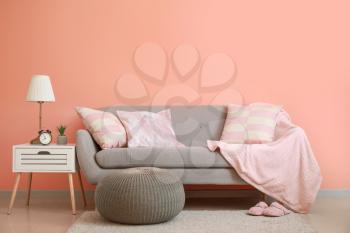 Cozy sofa with pouf and table near color wall in room�