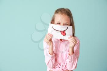 Little girl hiding mouth behind drawn smile on color background�