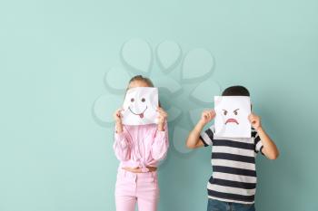 Little children hiding faces behind drawn emoticons on color background�