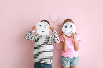 Little children hiding faces behind drawn emoticons on color background�