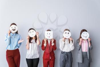 Group of woman covering their faces with drawn emoticons against light background�