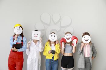 Group of female workers covering their faces with drawn emoticons against light background�