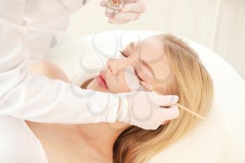 Young woman undergoing procedure of eyelashes dyeing in beauty salon�