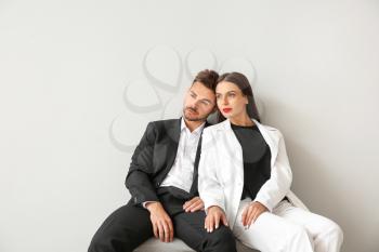Stylish young couple sitting on bench near white wall�