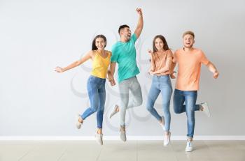 Group of jumping young people in stylish casual clothes near light wall�