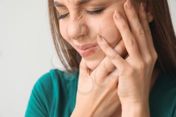 Young woman suffering from toothache against light background, closeup�