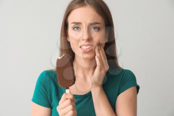 Young woman with sensitive teeth and cold ice-cream on light background�