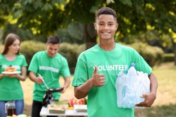 Young African-American volunteer with water for poor people outdoors�