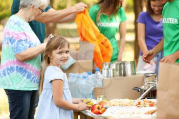 Little poor girl receiving food from volunteers outdoors�