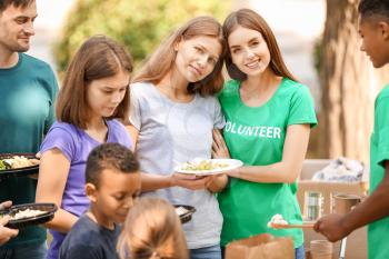 Young volunteers giving food to poor people outdoors�