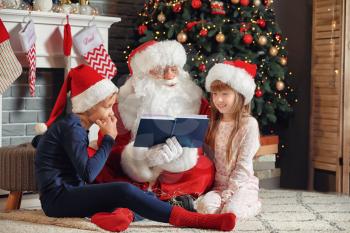 Santa Claus and little children reading book in room decorated for Christmas�