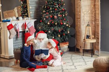 Santa Claus and little children reading book in room decorated for Christmas�