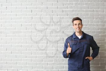 Male car mechanic showing thumb-up near brick wall�