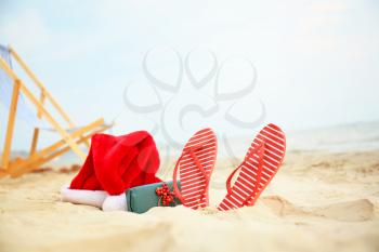 Santa Claus hat with gift box and flip-flops on sea coast. Christmas vacation�