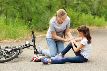 Mother helping her little daughter after falling off bicycle outdoors�