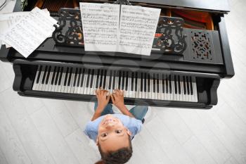 Little African-American boy playing grand piano at home, top view�