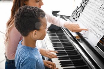 Woman teaching little African-American boy to play piano at home�